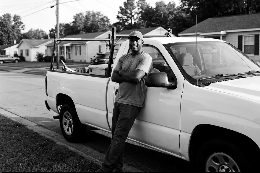 The owner of a family roofing company leaning on his work truck